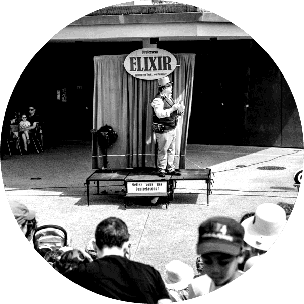 le spectacle de rue , the spectacular elixir magic show, le magicien bonimenteur se tient debouts sur son triporteur scénique face au public