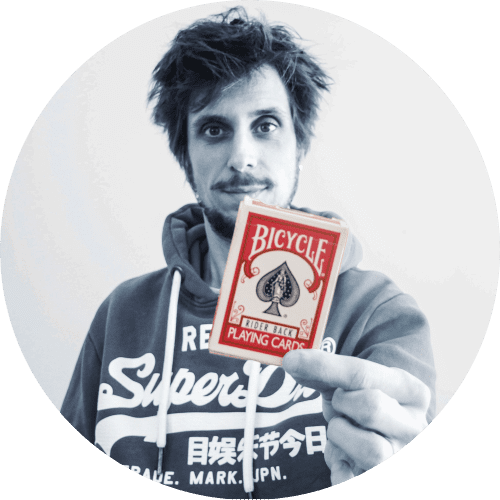 portrait de david silaguy, magicien humoriste de la compagnie des magicos à roulettes, la photo est en noir et blanc et le magicien présente un jeu de carte rouge au premier plan